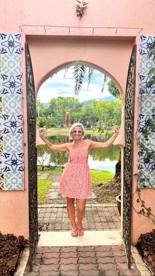 Willo standing in a pink doorway wearing a pink dress with a lush green background