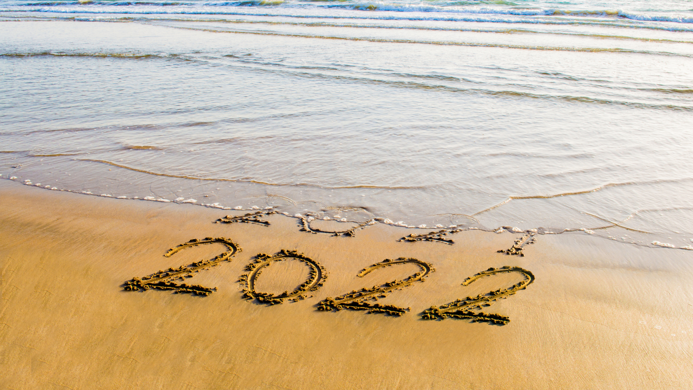 ocean washing away 2021 with 2022 written in the sand