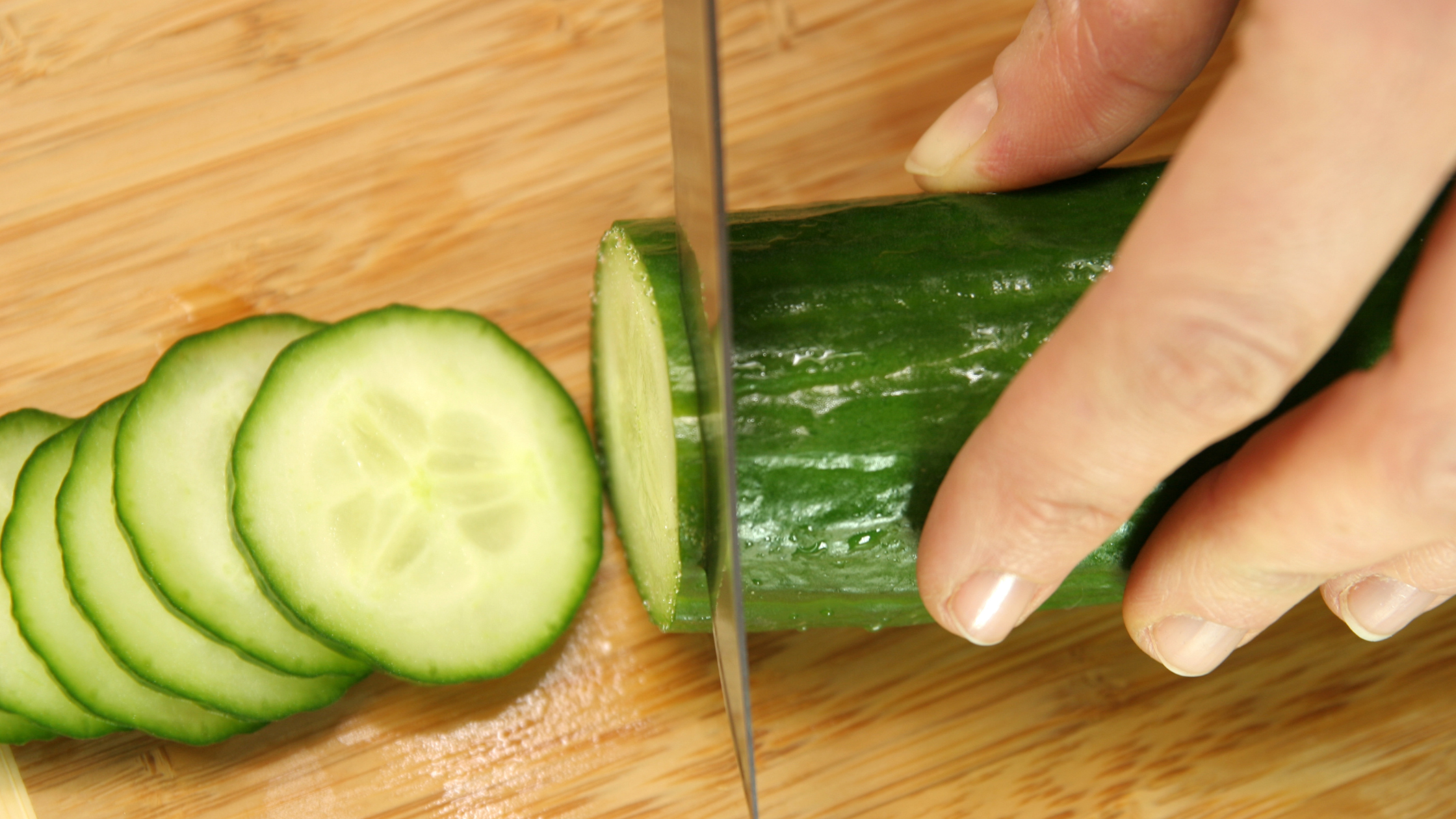 hand holding knife and cutting cucumber