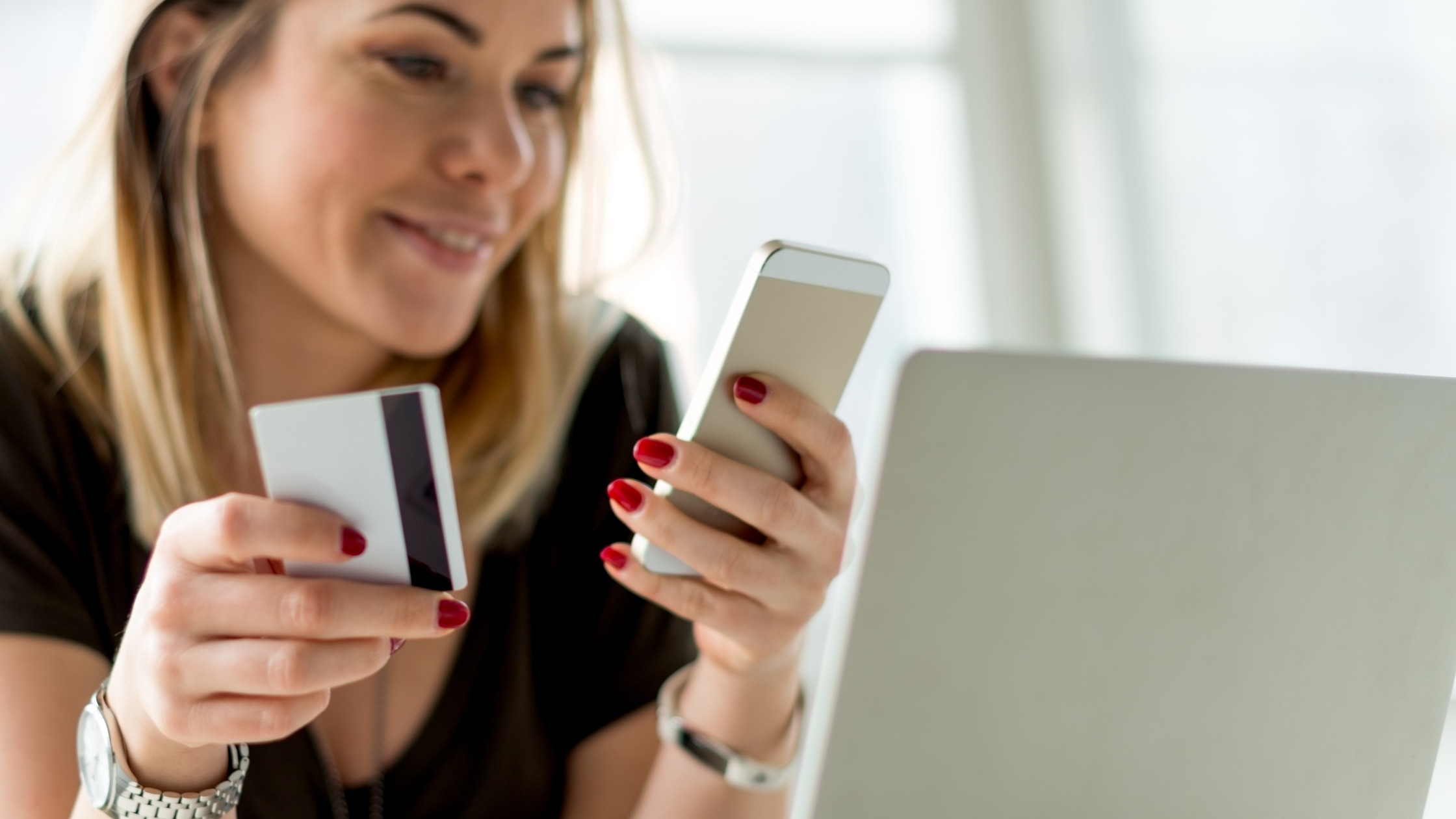 woman holding phone and credit card with laptop in front of her