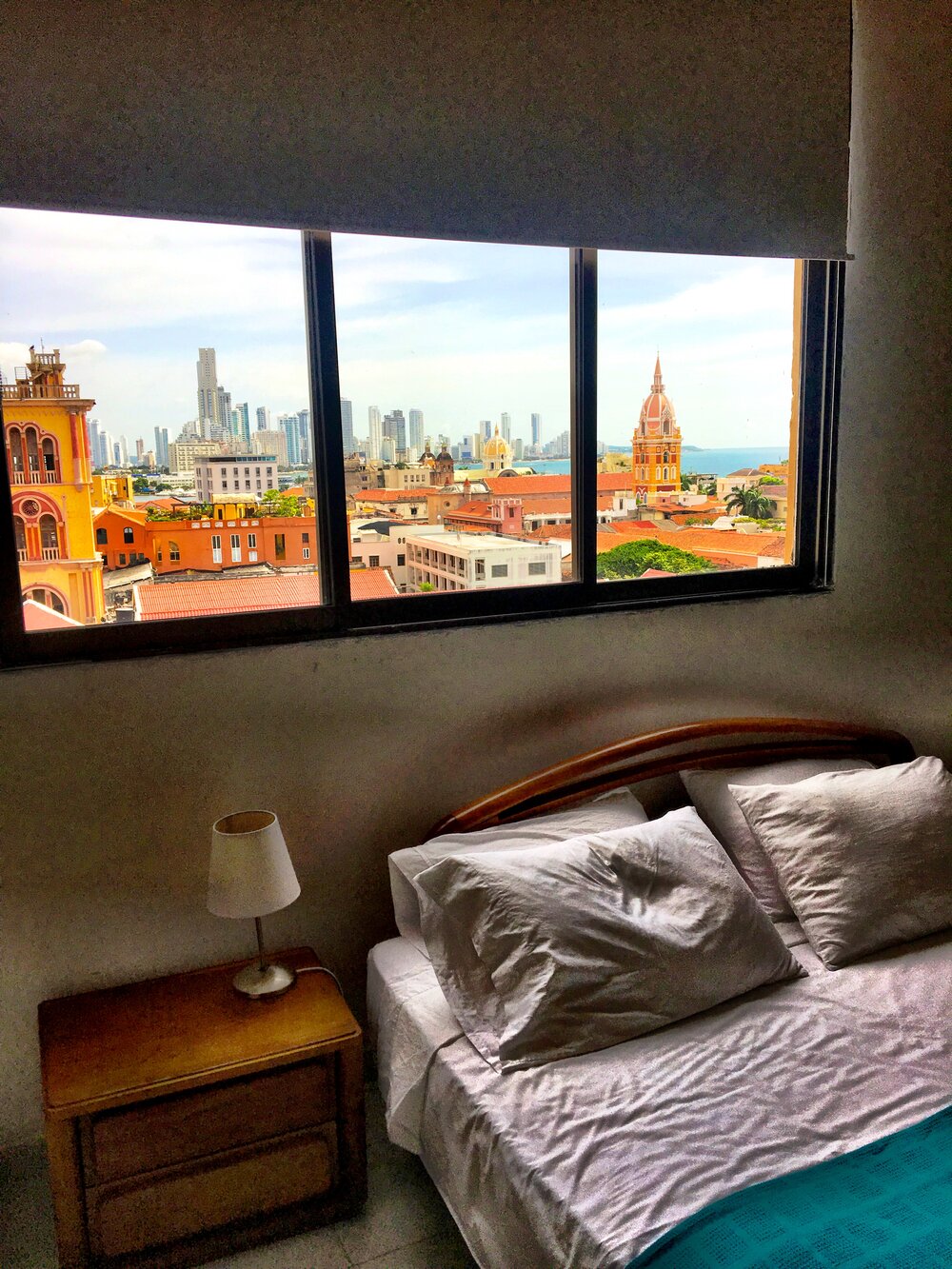 Bed and nightstand with a view from the window overlooking a city skyline