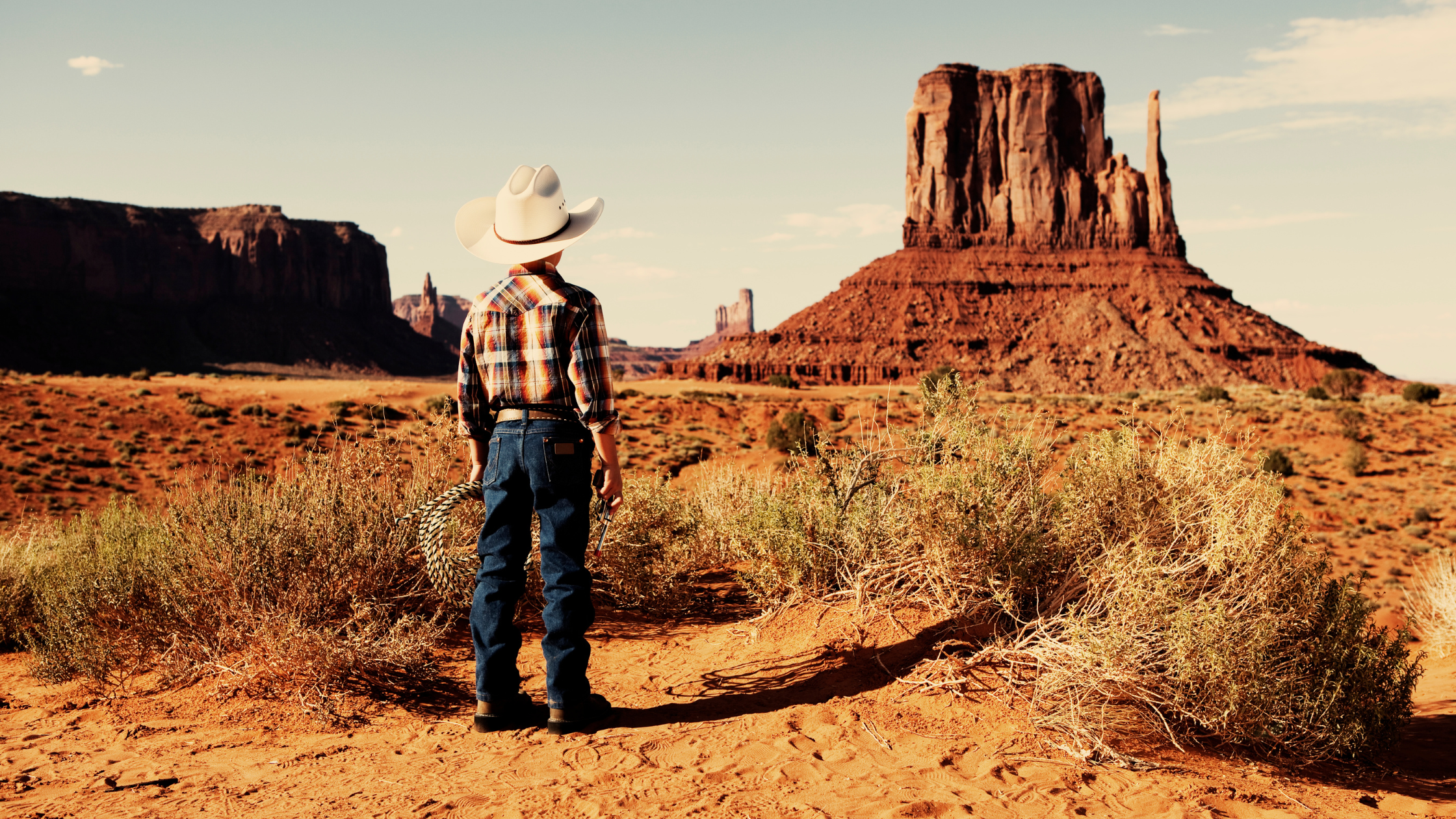 kid in western wear and white hat looking over desert landscape