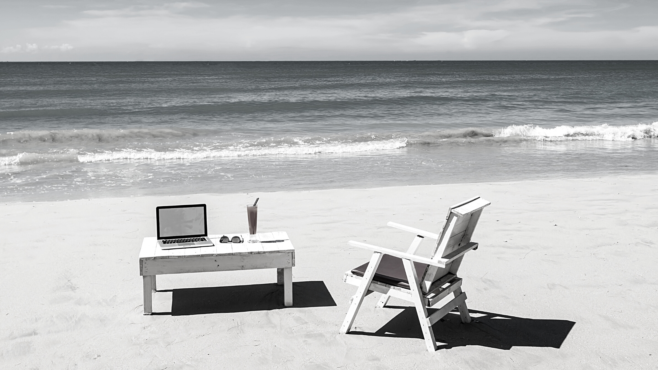 desk with laptop and chair set up on beach shore
