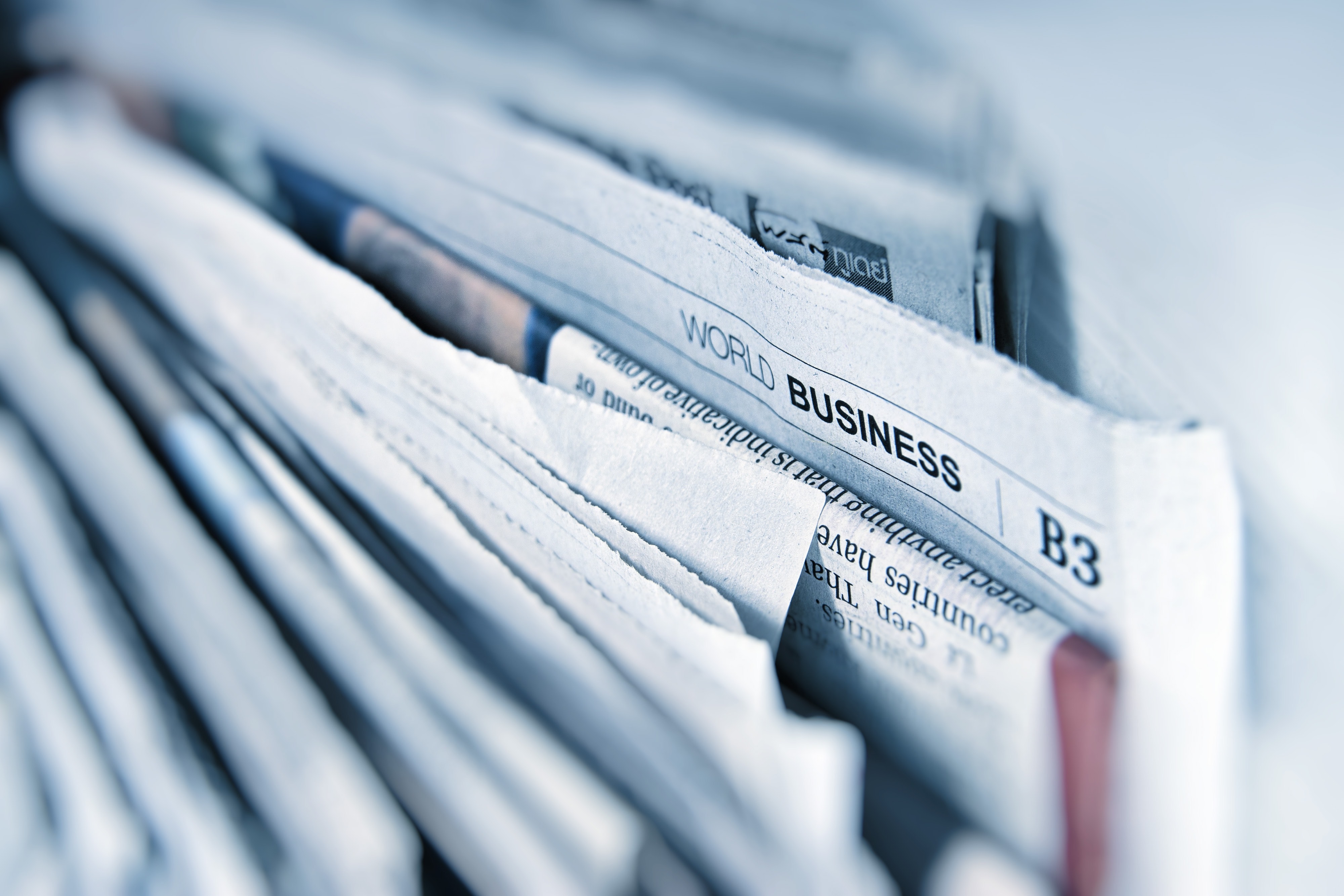 Several newspapers stacked together with the Business section visible